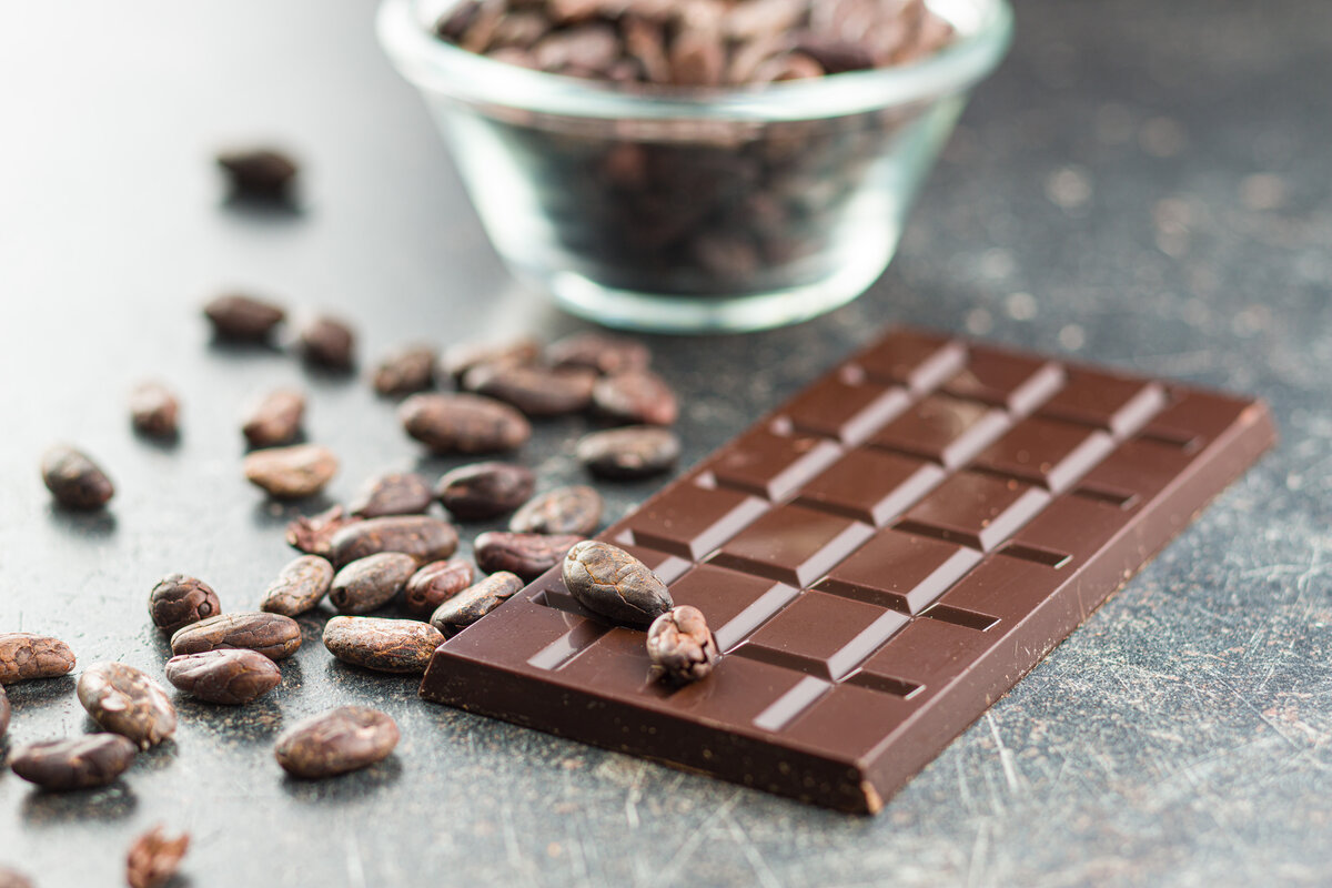 Dark organic chocolate bar and cocoa beans on kitchen table.