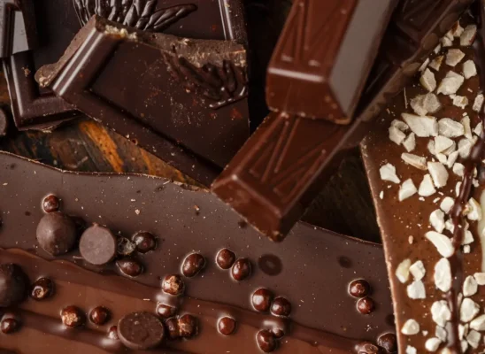 Top view of slices of dark and milk chocolate with chocolate chips on a brown background close-up