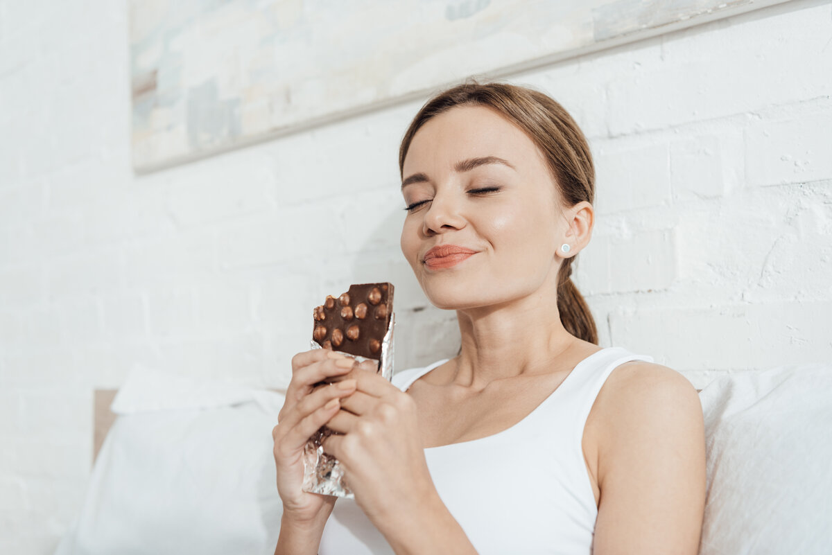low angle view of smiling young woman eating choco treat yourself