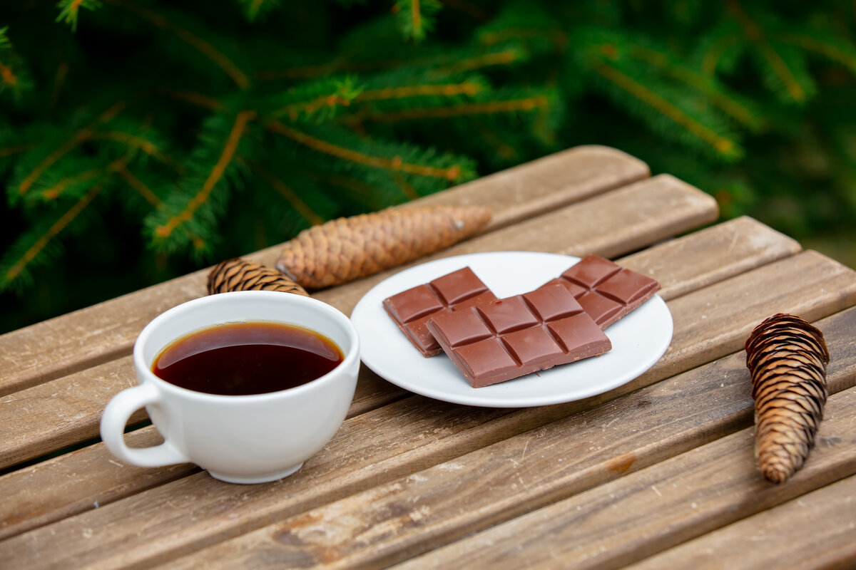 cup of coffee and chocolate bar on wooden table with spruce bran