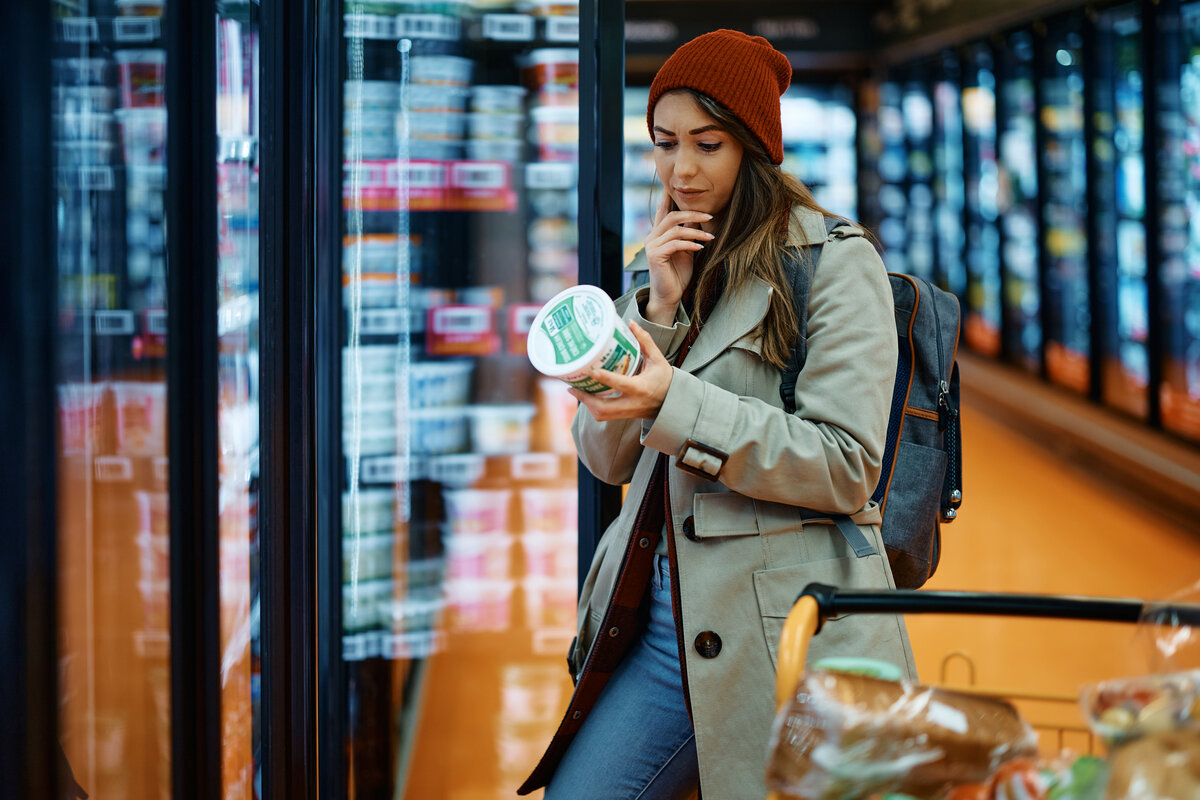 Young woman buying dairy product and reading food label in grocery store.